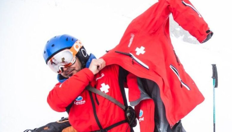 Un patrullero de Cerro Catedral se coloca la campera roja del uniforme, con nieve de fondo.