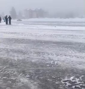 Playa de estacionamiento de tierra del cerro Catedral cubierta de nieve, con personas caminando y edificios de fondo entre la niebla