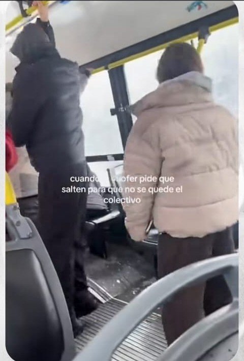 Pasajeros de pie en el fondo de un colectivo, en Bariloche, con nieve visible por la ventanilla