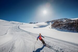 Un esquiador desciende por una pista recién pisada de la cordillera rionegrina, con cielo despejado y bosque nevado de fondo.