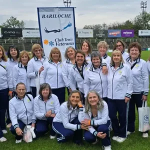 La delegación del Club de Tenis Veteranas Bariloche posa con el cartel del club en una cancha de Tucumán
